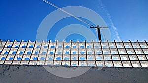 Frost on a metal wire fence against the background of an electric pole and blue sky