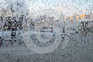 Frost patterns on a glass. Blurred city view through a frosted window. Concept of extremely cold weather conditions