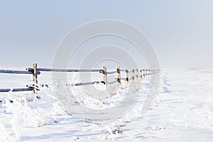 Frost and snow covered wooden fence in winter time.