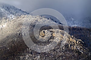 Frost on trees in a mountain forest, rock lit by the sun