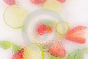 Frosted Glass with water drops with fruits behind it. Close-up of refreshing cocktail