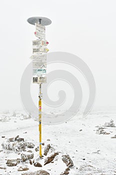 Frosted tourist signpost at the top of Mount Snieznik on a hiking mountain trail, winter landscape on a foggy day