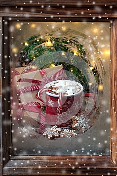 Frosted window with hot drink in mug and gingerbreaf cookies. Christmas greeting card