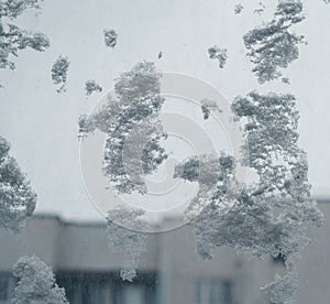 Frostwork. Decorative crystals of ice and snow on the window against the background of the city and sky. Frosty pattern. Ice