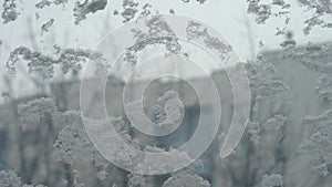 Frostwork. Decorative crystals of ice and snow on the window against the background of the city and sky. Frosty pattern. Ice