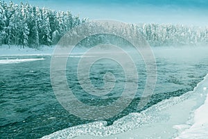 Frosty fog over winter river with snow and forest on bank. First ice on lake