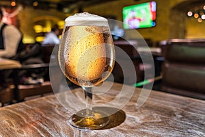 Frosty glass of light beer on the bar counter. Pub interior at the background