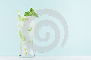 Frosty mint lemonade with green leaf, ice cubes, striped straw, mineral water in elegant glass on white wood table, mint color.