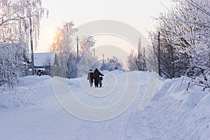 Frosty morning at the village. Couple is walking along the snowy countryside road