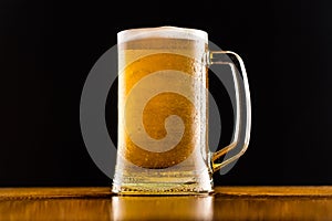 Frosty mug of beer close up on wooden table against black background.