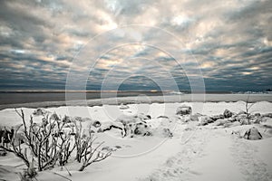 A frosty weather landscape of cloud covered sky and snow covered half frozen lake in northern Europe with pine trees