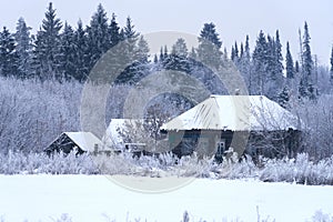 A frosty winter day. A farmer\'s remote snow-covered dwelling on the edge of the forest. Trees in white hoarfrost.