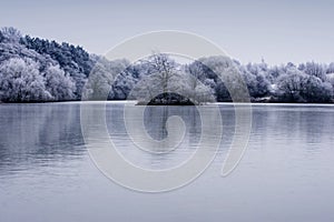 Frosty winter trees landscape with reflection in lake