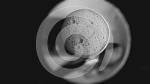 Froth bubbles on top of cup full of milk in black and white