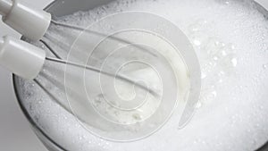 Frothing and whipping milk product with the whisk of a mixer in a gray bowl.