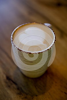 A frothy cappuccino cup with on a heart as a coffee art on a wooden table
