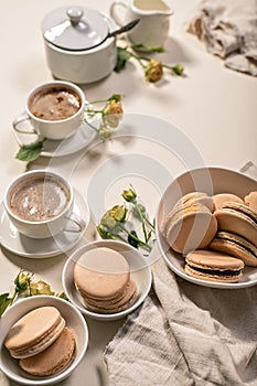 Frothy coffee in white cups, delicious French macaroons. Dessert still life on a beige background. Vertical shot