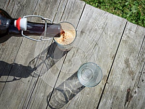 Frothy dark beer pouring into tall glasses from a brown glass bottle in summer garden on rustic wooden table