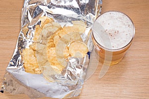 Frothy pint of lager and open bag of potato chips