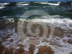 Frothy waves of the sea on the sandy beach. Foamy wave rolls