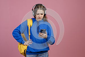 Frown schoolgirl standing, using smartphone, looking.