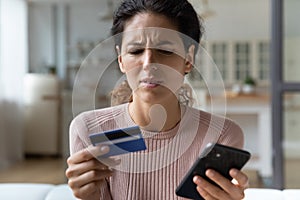 Frown woman holding card and cellphone experiences problems with e-payment