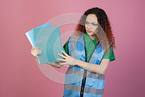 Frown, young female with red, curly hair posing indoors, holding folders, showing.