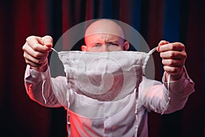 Frowned man in white shirt holding gauze mask in hands on dark background. Emotion of anger and determination. Healthcare, respira photo