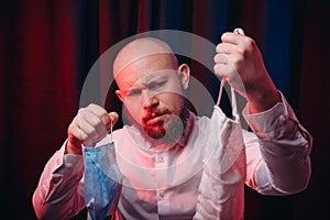 Frowned man in white shirt holding gauze masks in hands on red and blue background. Emotion of assertiveness and determination