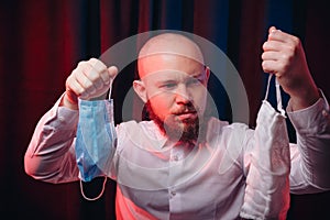 Frowned man in white shirt holding gauze masks in hands on red and blue background. Emotion of assertiveness and determination