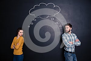 Frowning angry couple thinking identically over background of chalkboard