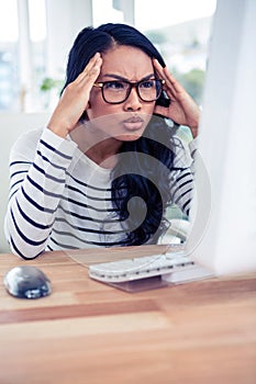 Frowning Asian woman looking at computer monitor with hands on head