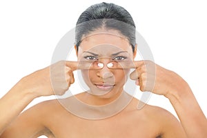 Frowning black haired model pressing blackhead on her nose