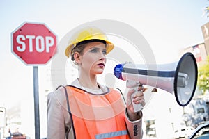 Frowning businesswoman wearing builders clothes holding megaphone