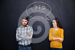 Frowning couple standing after argument over chalkboard background