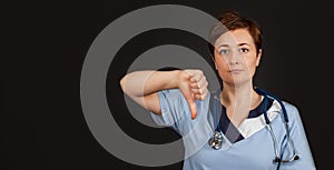 Frowning doctor woman showing disapproval sign-holding thumb down