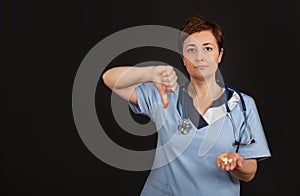 Frowning doctor woman showing disapproval sign-holding thumb down