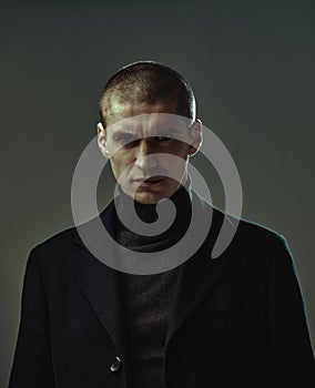 Frowning handsome angry man in black suit security or criminal on gray background, studio male portrait with copy space