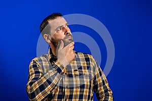 Frowning man thinking expressing doubts and concerns. Hipster male with beard in blue plaid checkered shirt Isolated on