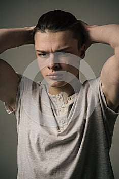 Frowning teenage boy isolated on gray background, street, hooligan, troublemaker. Young man with muscular torso and