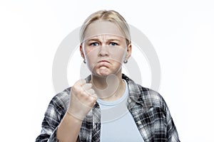 Frowning teenage girl shows her fist. A cute blonde with freckles on her face wearing a plaid shirt and a blue top. Negative