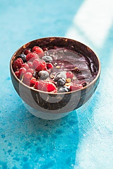 Frozen acai smoothie in coconut shell with raspberries, banana, blueberries,  fruit and granola on concrete background. Breakfast