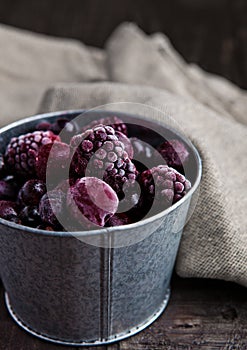 Frozen berries mix in a black bowl on wooden background