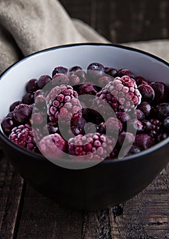 Frozen berries mix in a black bowl on wooden background