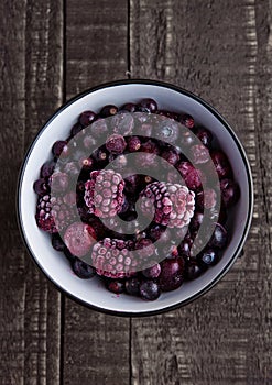 Frozen berries mix in a black bowl on wooden background