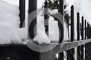 Frozen black metal fence covered with snow