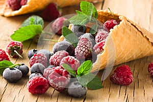 Frozen blueberries berries raspberries in a waffle cone, fresh cherries on old wooden table - right side view