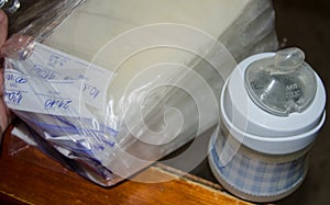 Frozen breastmilk in storage bags and baby bottle with fresh expresed breast milk on wooden table