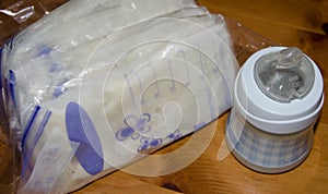 Frozen breastmilk in storage bags and baby bottle with fresh expresed breast milk on wooden table