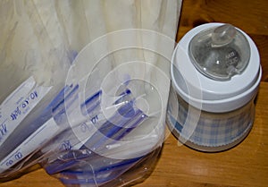 Frozen breastmilk in storage bags and baby bottle with fresh expresed breast milk on wooden table